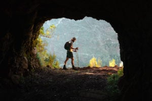 a man with a backpack and trek poles standing in a cave.