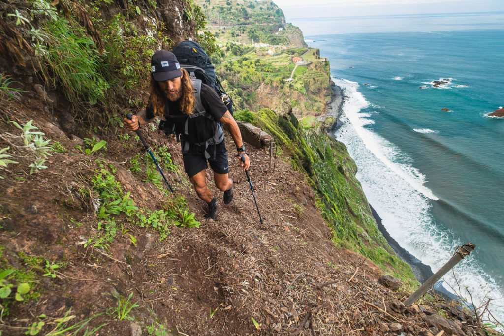 a man hiking up a steep hill next to the ocean.