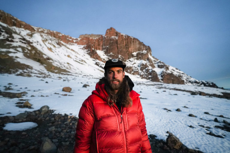 a man in a red jacket standing in front of a mountain.