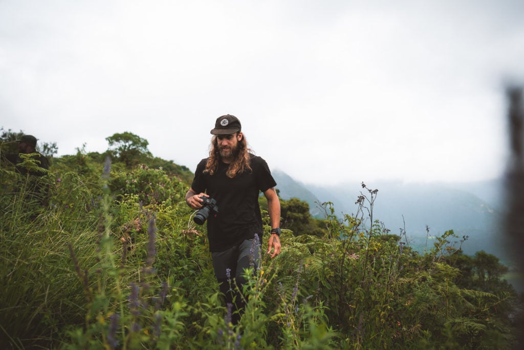 a man with long hair and a hat walking through tall grass