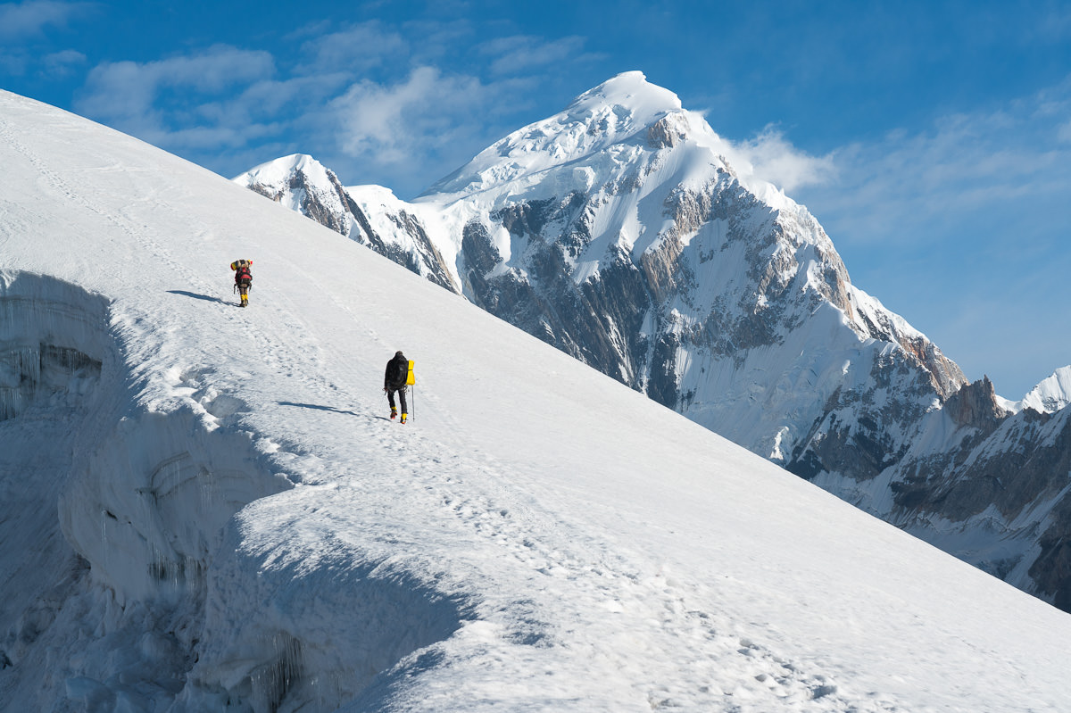 two people walking up the side of a snow covered mountain