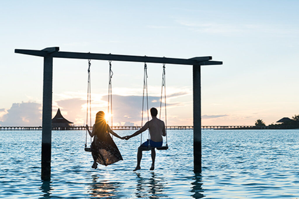 a man and a woman holding hands on a swing in the water