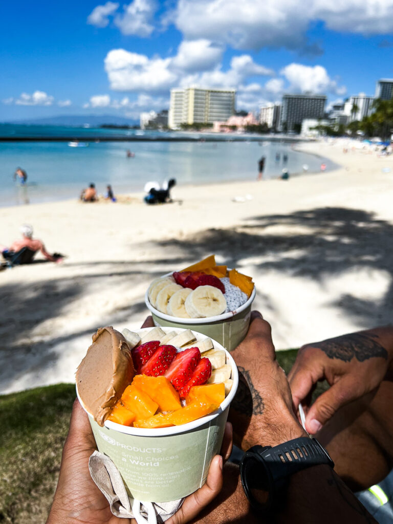 a man holding two cups of fruit on a beach