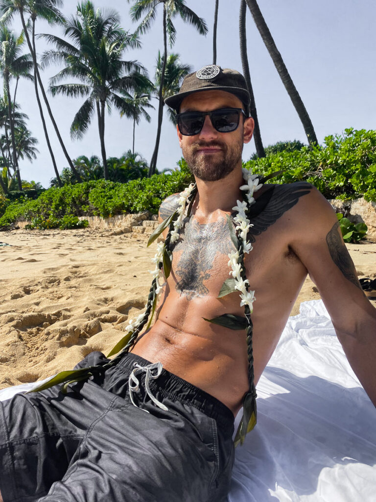 a shirtless man sitting on a beach with palm trees in the background