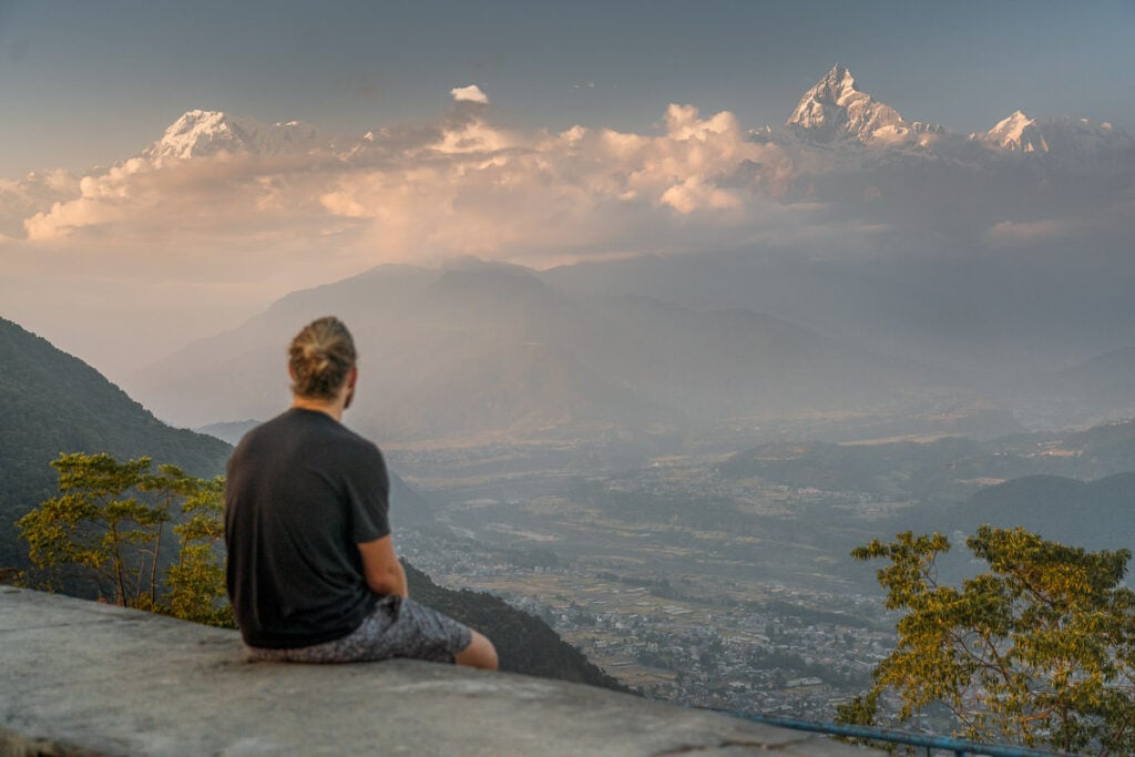a man sitting on a ledge looking at the mountains