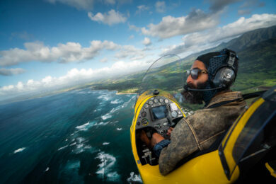 a man flying a yellow airplane over the ocean.