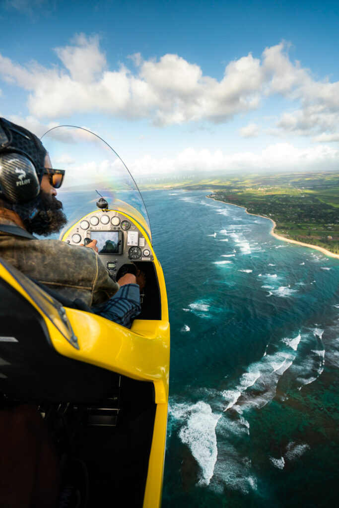 a man flying a yellow plane over the ocean.