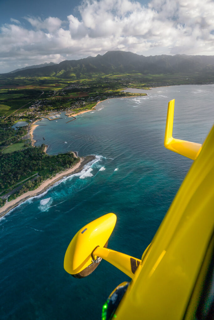 a yellow airplane flying over the ocean next to a beach.
