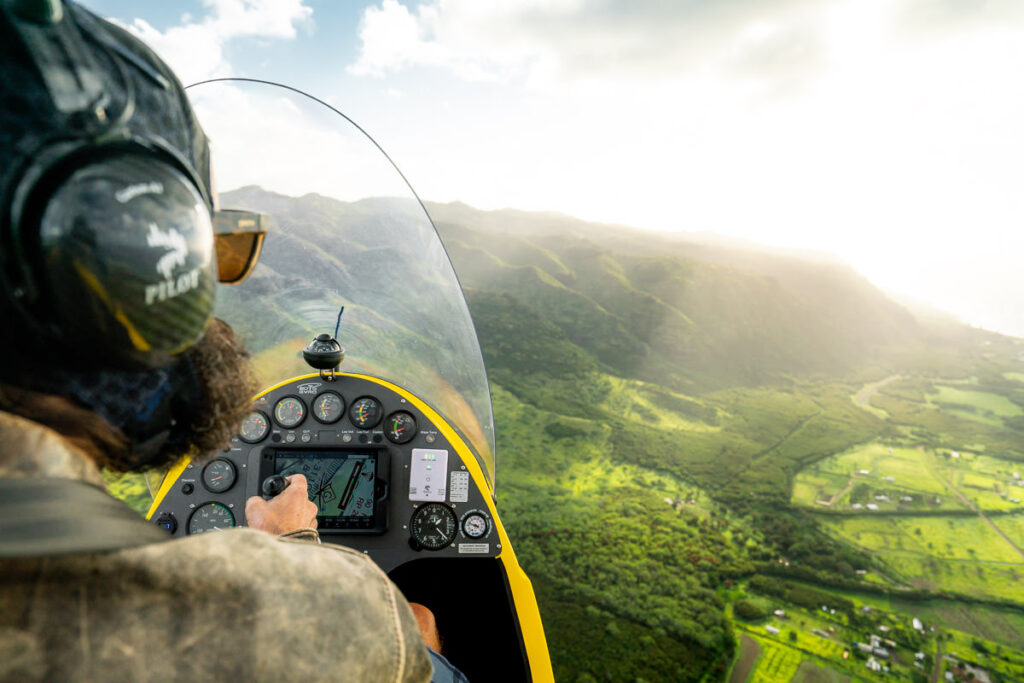 a man flying a small plane over a lush green hillside.