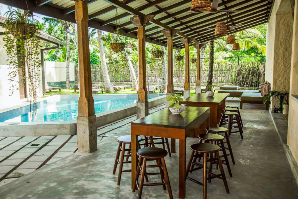 An eco lodge in Sri Lanka featuring a patio with a table and chairs and a pool in the background.