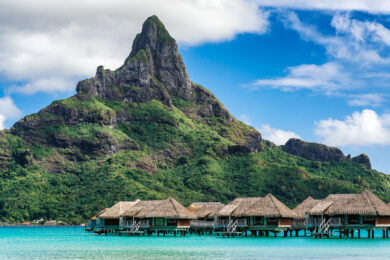 A cluster of overwater bungalows in French Polynesia perched atop a beach and mountain.