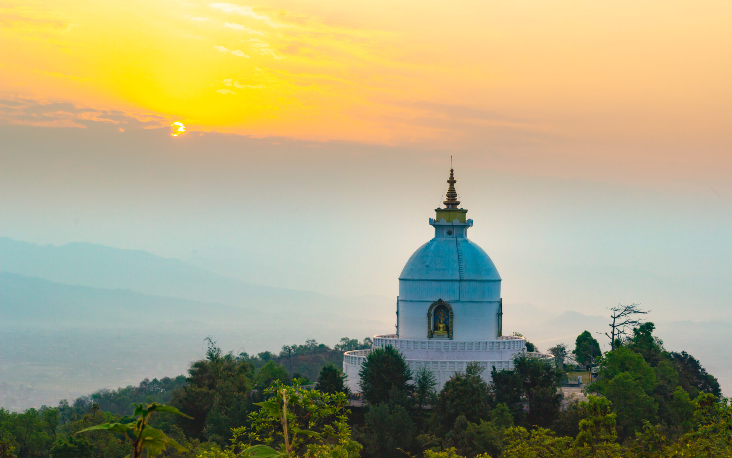 Description modified: A white pagoda in Kathmandu sits on top of a hill at sunset.