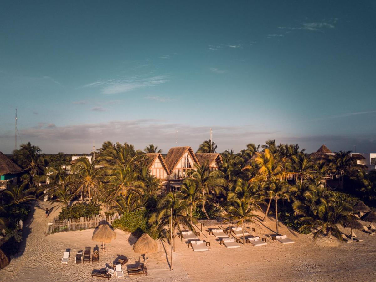 La Valise Tulum 4 A tranquil beachfront at luxury resorts in Tulum, Mexico, with sun loungers, thatched umbrellas, and tropical foliage at sunset.