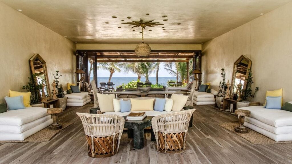 Luxury beachfront living room with open walls, rustic decor, and ocean view in Tulum, Mexico.