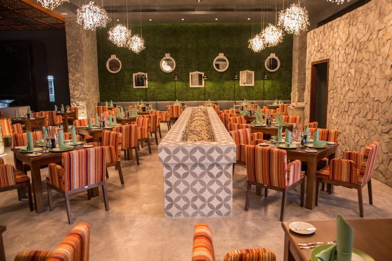Royalton Riviera Cancun, An Autograph Collection All-Inclusive Resort & Casino 2 A modern restaurant interior with stone walls, green foliage, hanging lights, multiple tables, orange and striped chairs, and a central structure decorated with geometric tiles—an ambiance that rivals any spot in *where to stay in Cancun*.