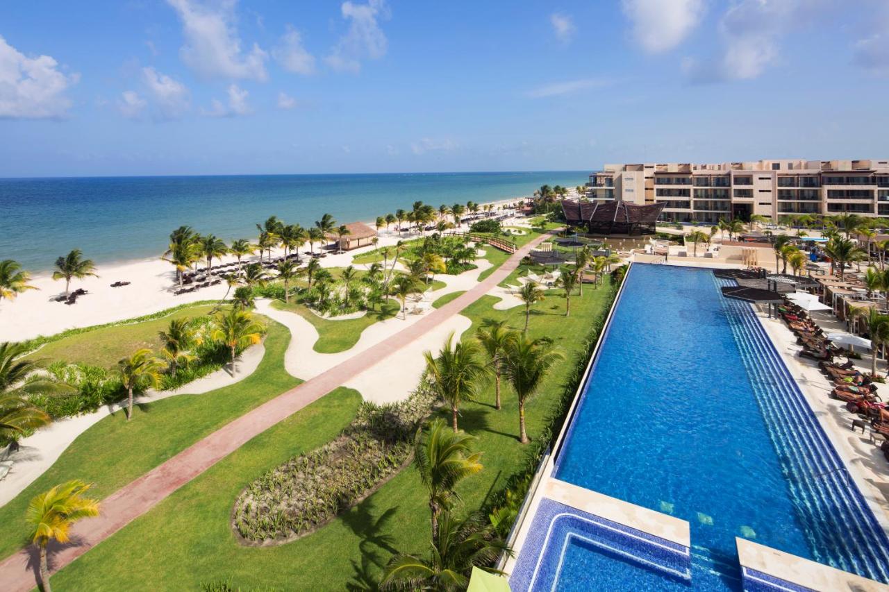 Royalton Riviera Cancun, An Autograph Collection All-Inclusive Resort & Casino An aerial view of a beachfront resort in Cancun showcases lush greenery, a long swimming pool, palm trees, and a sandy beach leading to the ocean—an ideal snapshot for anyone wondering where to stay in Cancun.