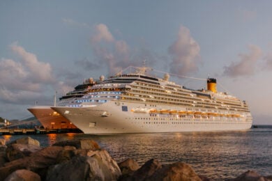 Two large cruise ships docked at a harbor during sunset, with calm water and rocky shoreline in the foreground.