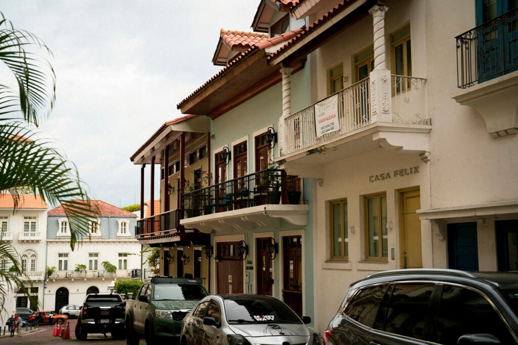 Cars parked along a narrow street lined with colorful, historic buildings featuring balconies and decorative details.