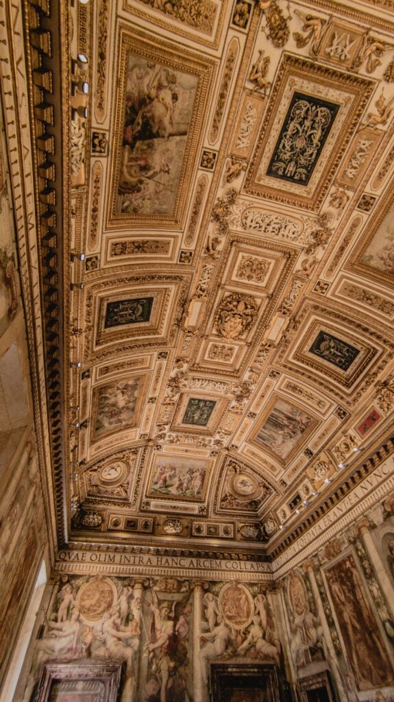 Ornate ceiling with detailed gold trim, classical paintings, and Latin inscriptions in a richly decorated historical room.