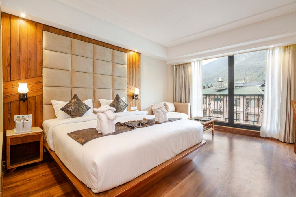 Hotel room featuring a king bed with two towel elephants, a padded headboard, and a large window overlooking a mountain landscape.