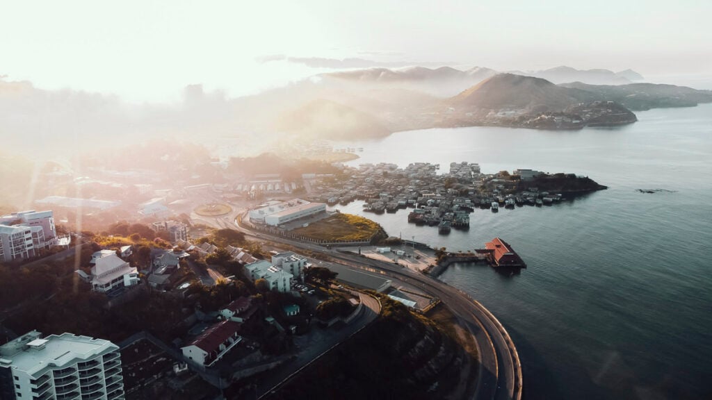 Aerial view of a coastal town and stilt houses over the water at sunrise.